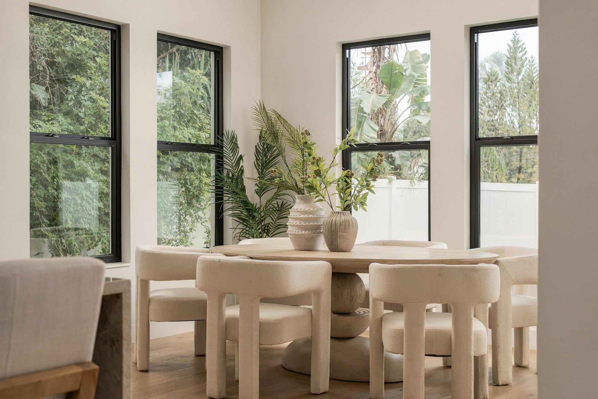 Dining table with sculptural boucle chairs beside tall black-framed windows